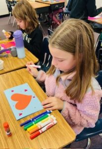 A student working on a a blue valentines day card with red hearts for veterans