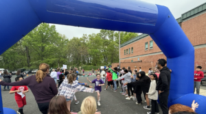 A student running through the finish line, greeted by high fives from other students and staff as they finish the fun run